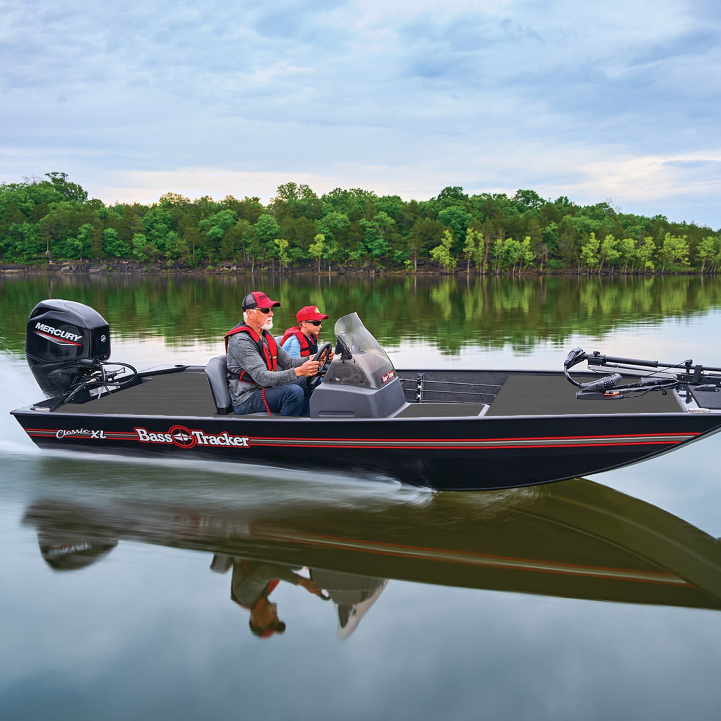 Two people boating on a Bass Pro Tracker bass boat with a Mercury outboard motor on a calm lake with a tree-lined shore in the background with DEKit Anchor Gray DIY foam boat flooring